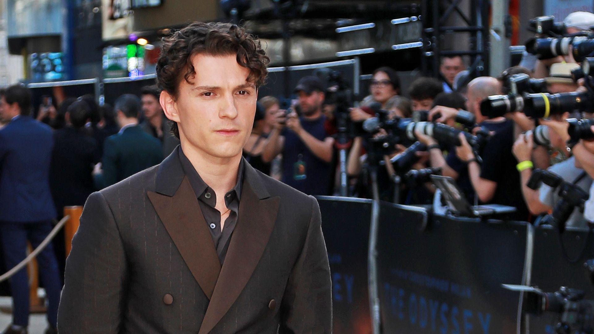 Tom Holland at an Odysseus premiere wearing a black suit and black shirt