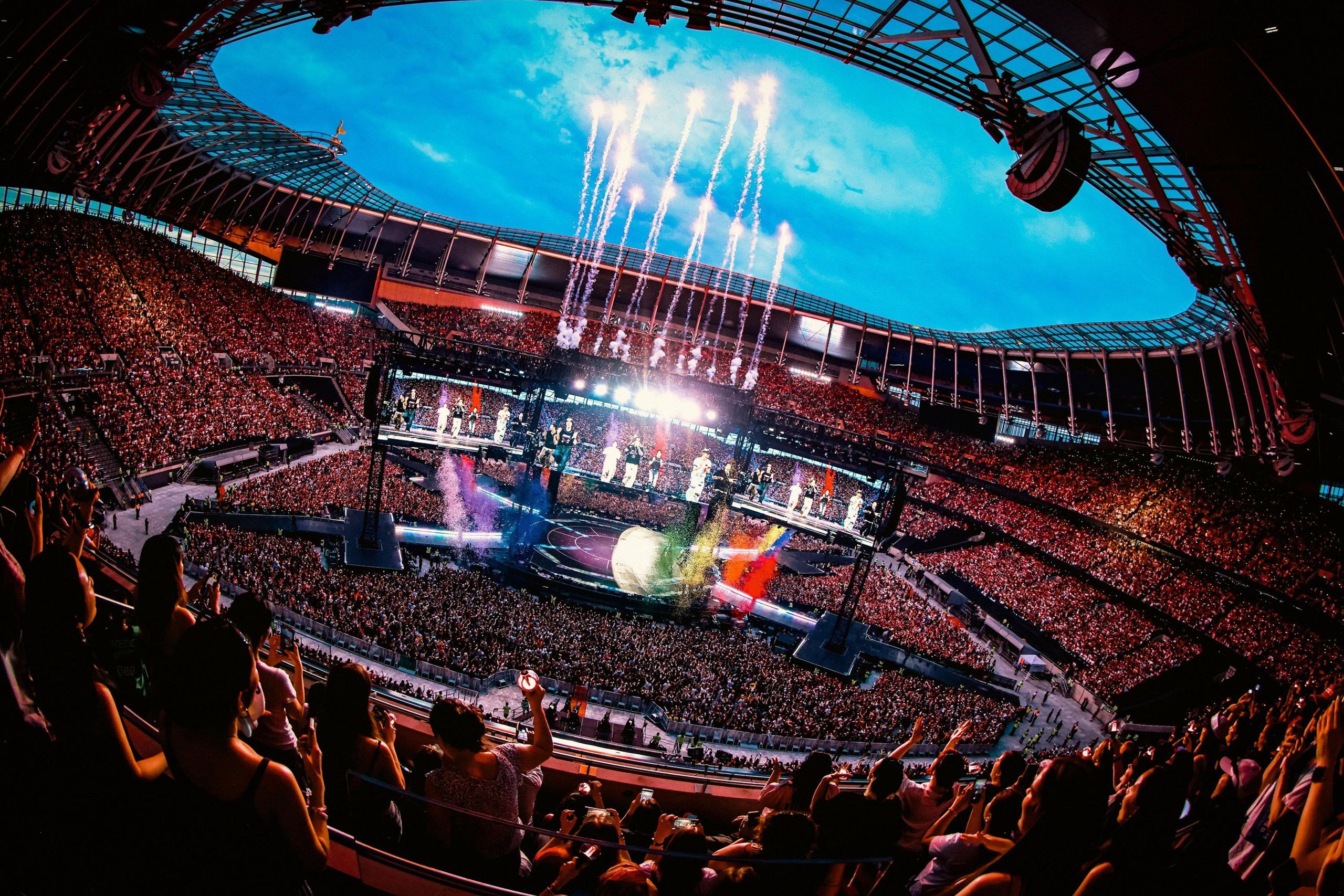 A wide shot of BTS performing in London, with thousands of fans watching as confetti and fireworks shoot into the sky