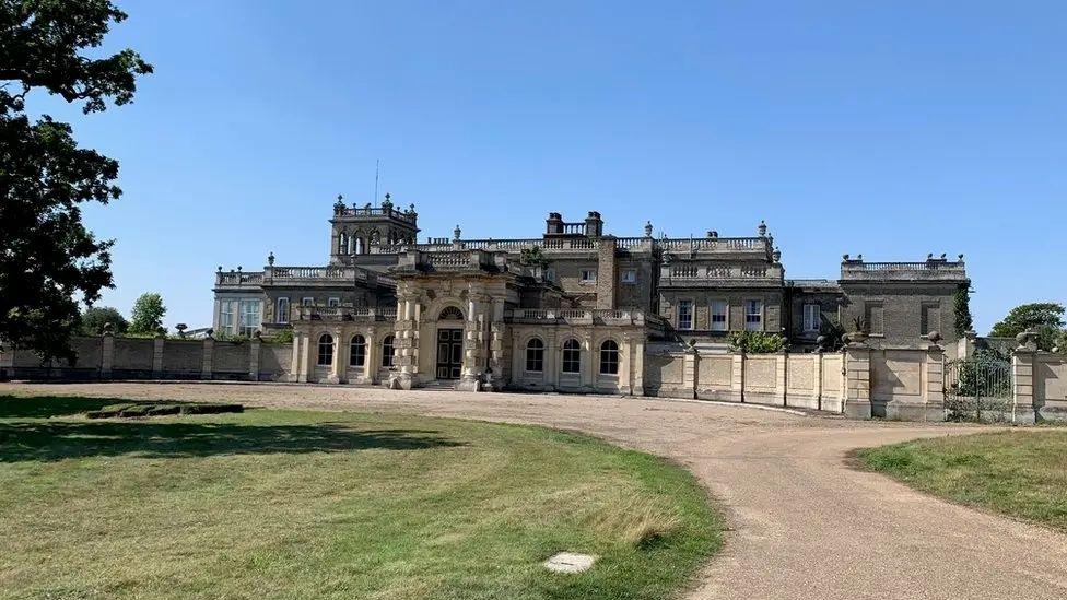 Shrubland Hall is a large historic building which has a large driveway in front of it. The building has a main entrance in the middle.