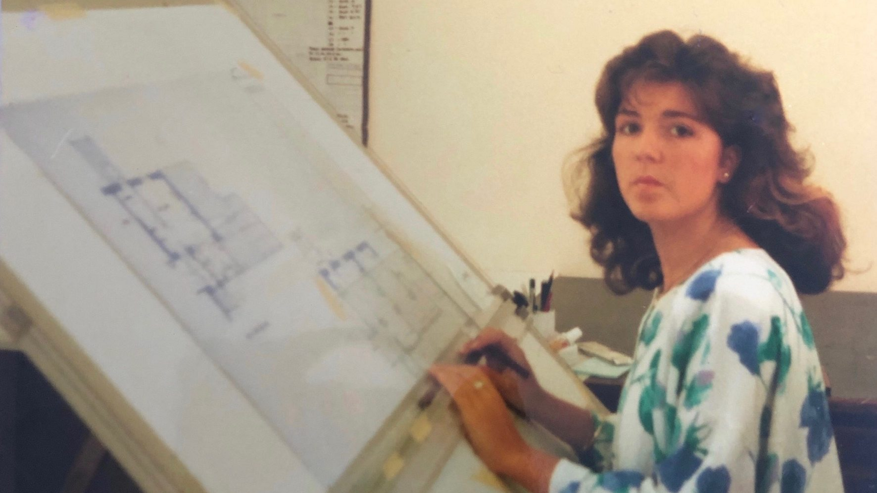 Lianne with long brown hair sat in front of a board with planning building designs on it.