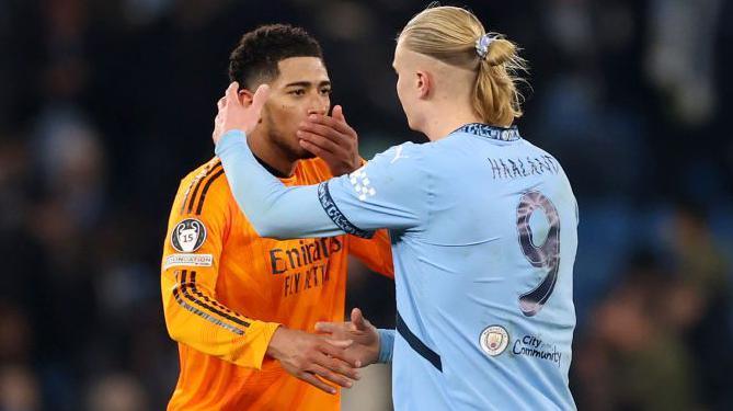 Jude Bellingham covers his mouth talking to Erling Haaland who is about to hug him