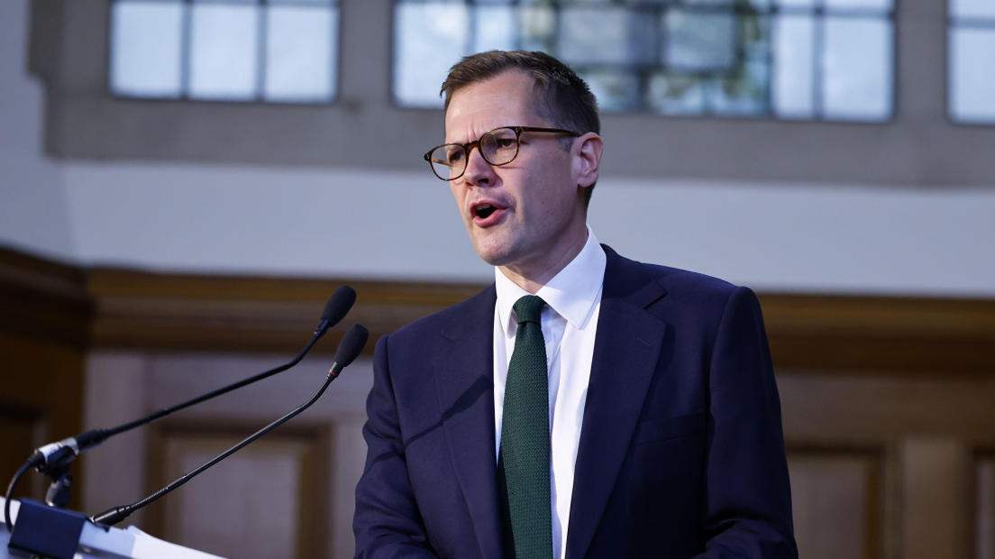 Reform UK's Robert Jenrick mid-speech. He is wearing glasses, has short, dark hair and is wearing a collared shirt and suit with a green tie.