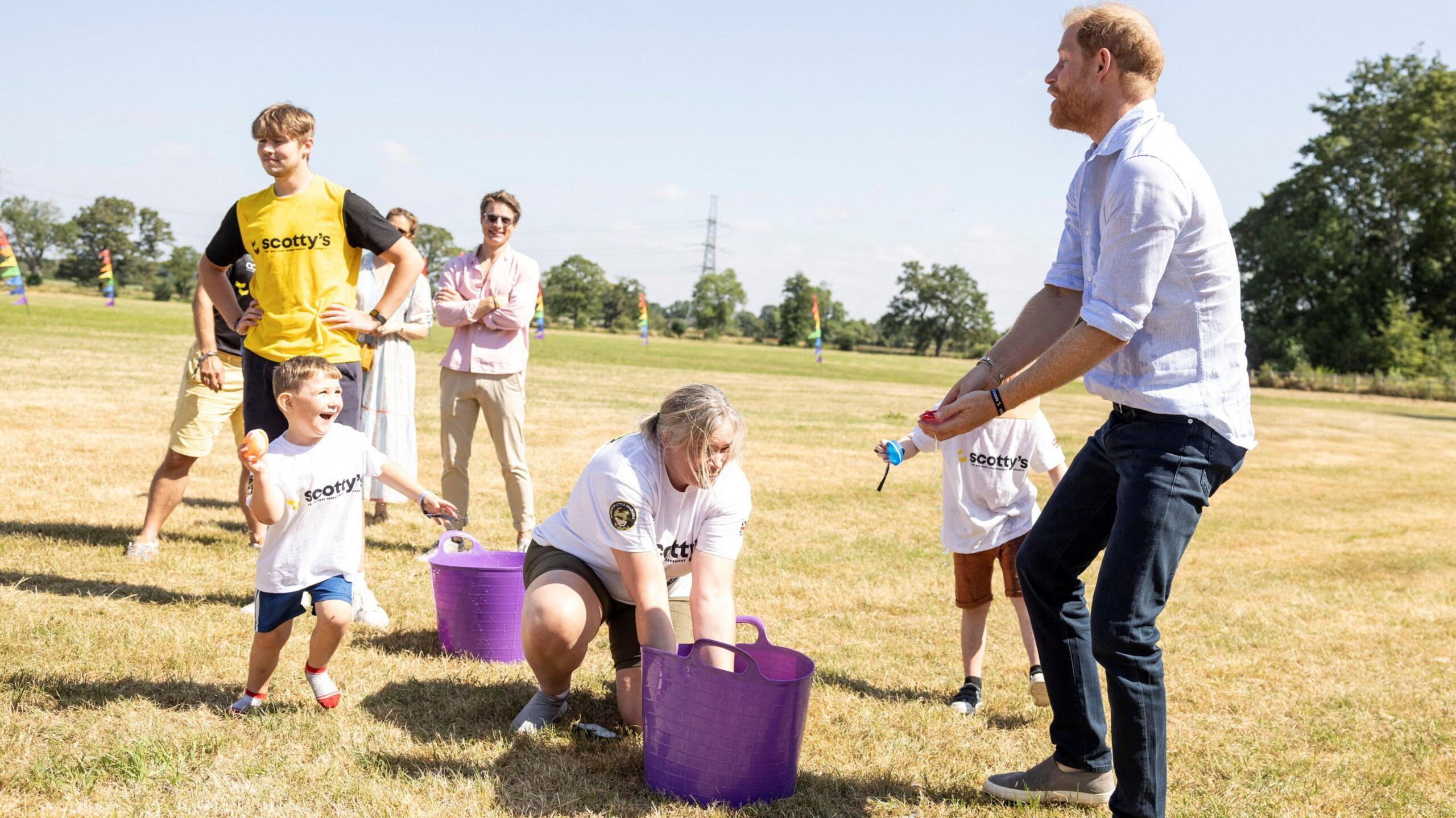Prince Harry prepares to be struck by a water bomb thrown by a young boy.