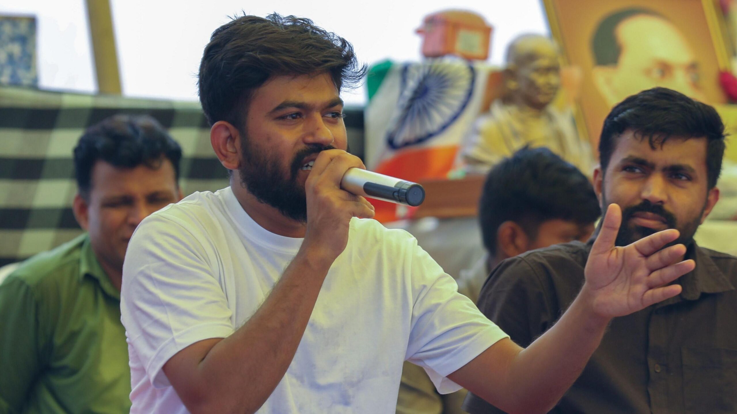 Abhijeet Dipke wears a white shirt, holding a microphone and speaking