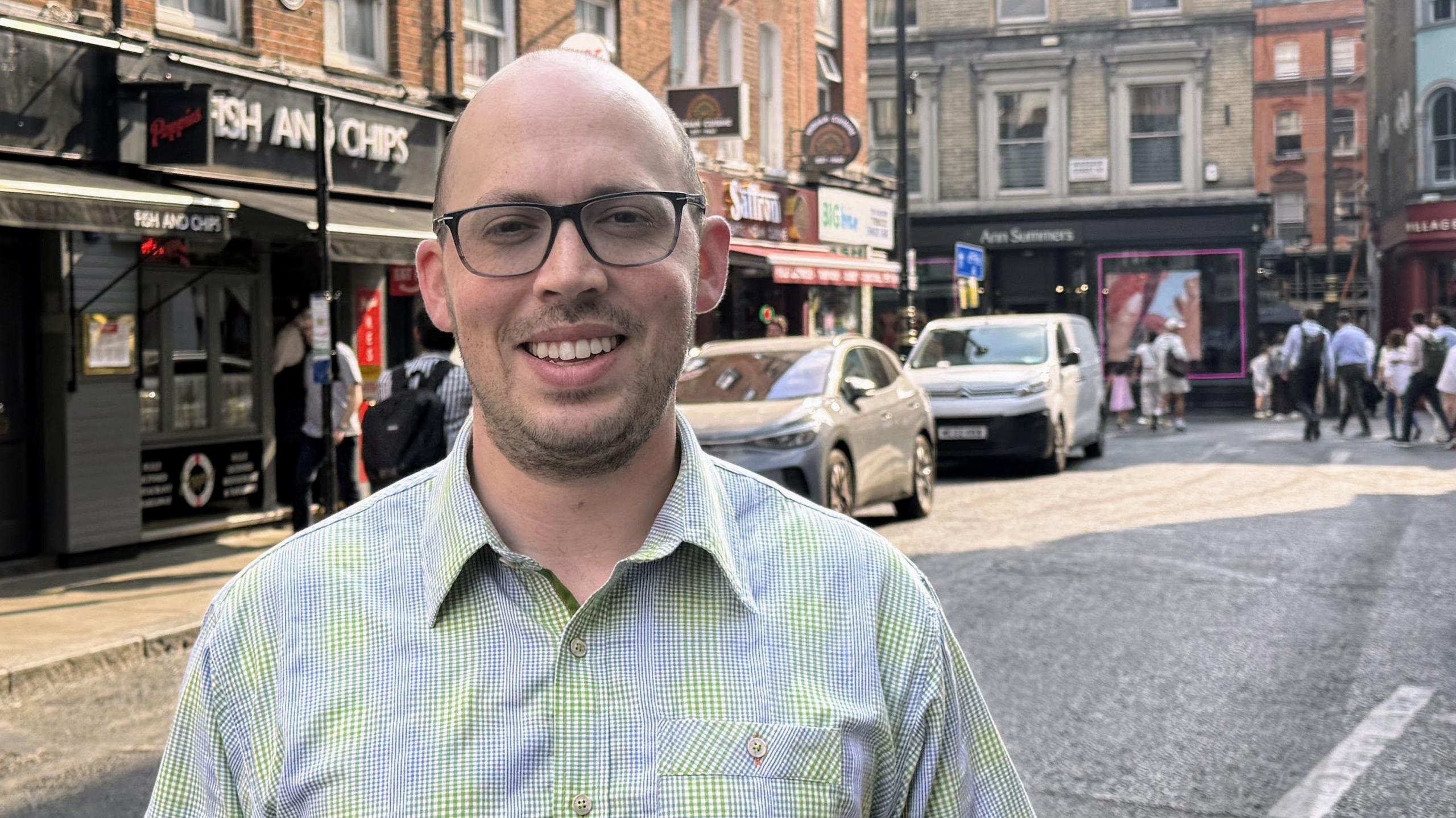 Matt Cohen stands in a street in London's Soho, wearing glasses and checked shirt