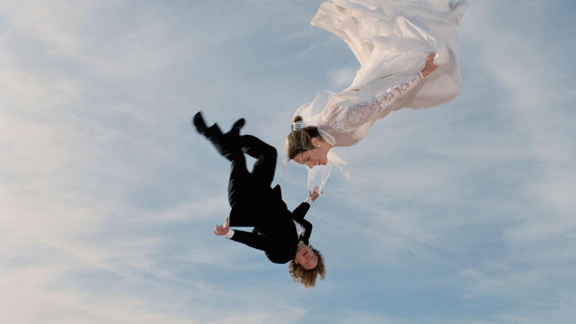 A skydiving couple, with man in a morning suit and the woman wearing a wedding dress