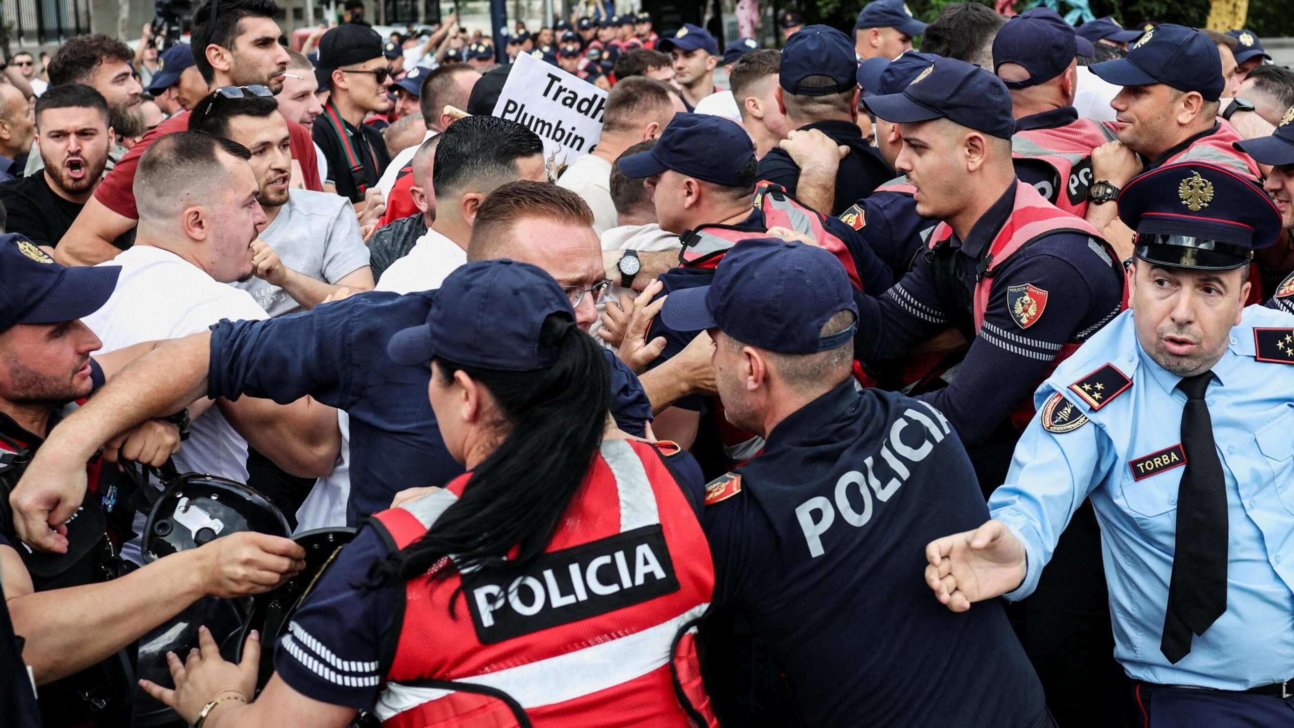 A crowd of demonstrators clash with police during a protest. Officers in red and blue uniforms which say 'POLICIA' hold back male protesters.