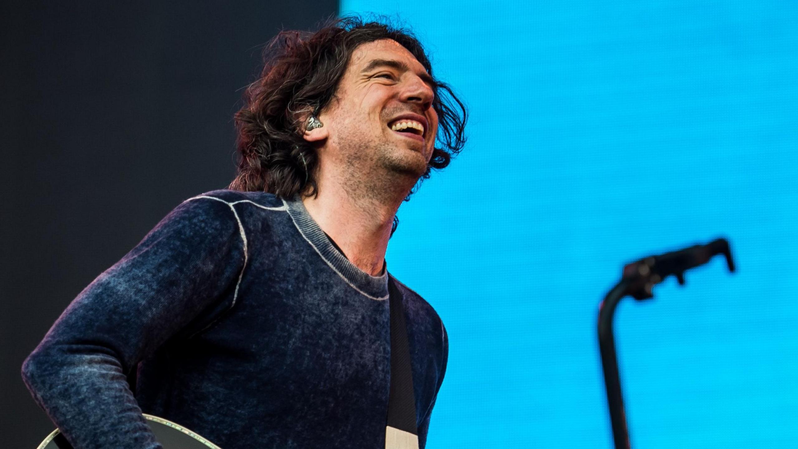 Gary Lightbody of Snow Patrol smiles as he performs on stage at the Latitude Festival in 2025, against a light blue backdrop