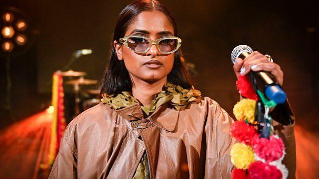 A woman wearing sunglasses holds a microphone in her hand.