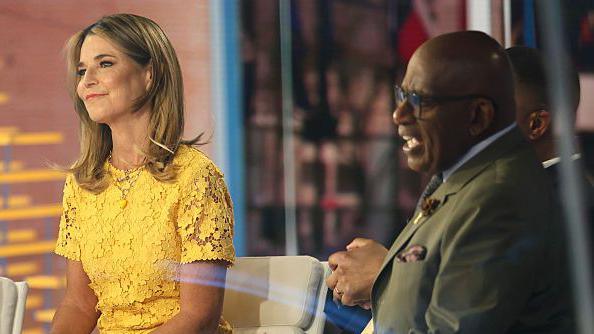 Savannah Guthrie, in a bright yellow dress with a lace floral pattern, smiles as she  sits next to Al Roker on the "TODAY" show set