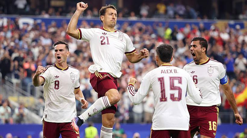 Mikel Oyarzabal jumps to celebrate scoring a penalty against France, wearing Spain's change kit of white shirt and burgundy shorts