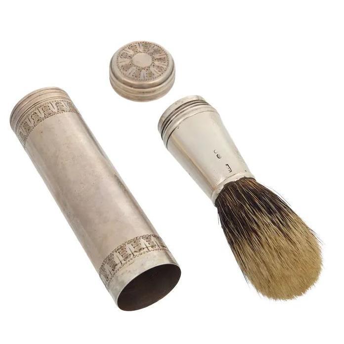 A silver cylinder with a lid  and a silver shaving brush.