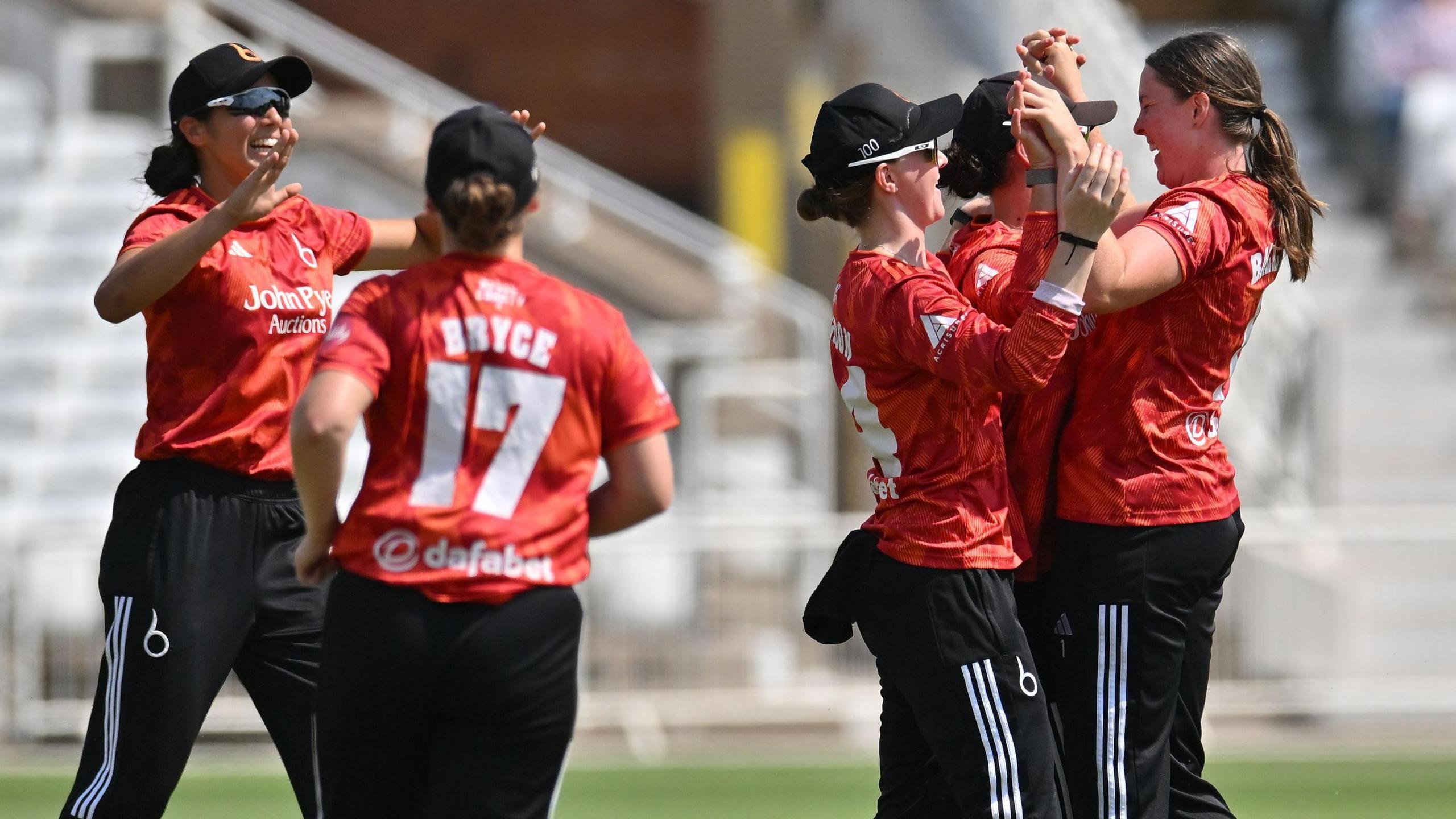 The Blaze team-mates celebrate a wicket in a T20 Blast feature. Kirstie Gordon high fives Grace Ballinger as Emma Jones runs towards them smiling. They are wearing The Blaze's 2026 T20 kit.