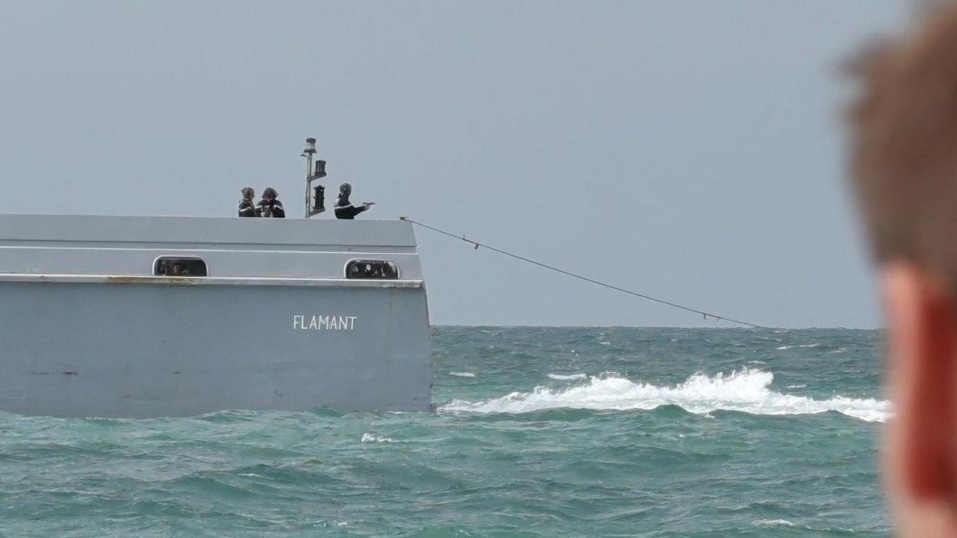 A French patrol officer at the back of the boat pointing a pistol towards the sea