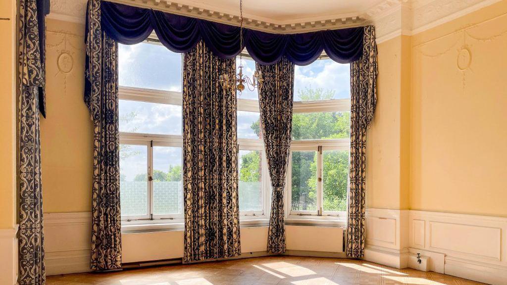 A high-ceilinged room in an Edwardian home with ornate curtains