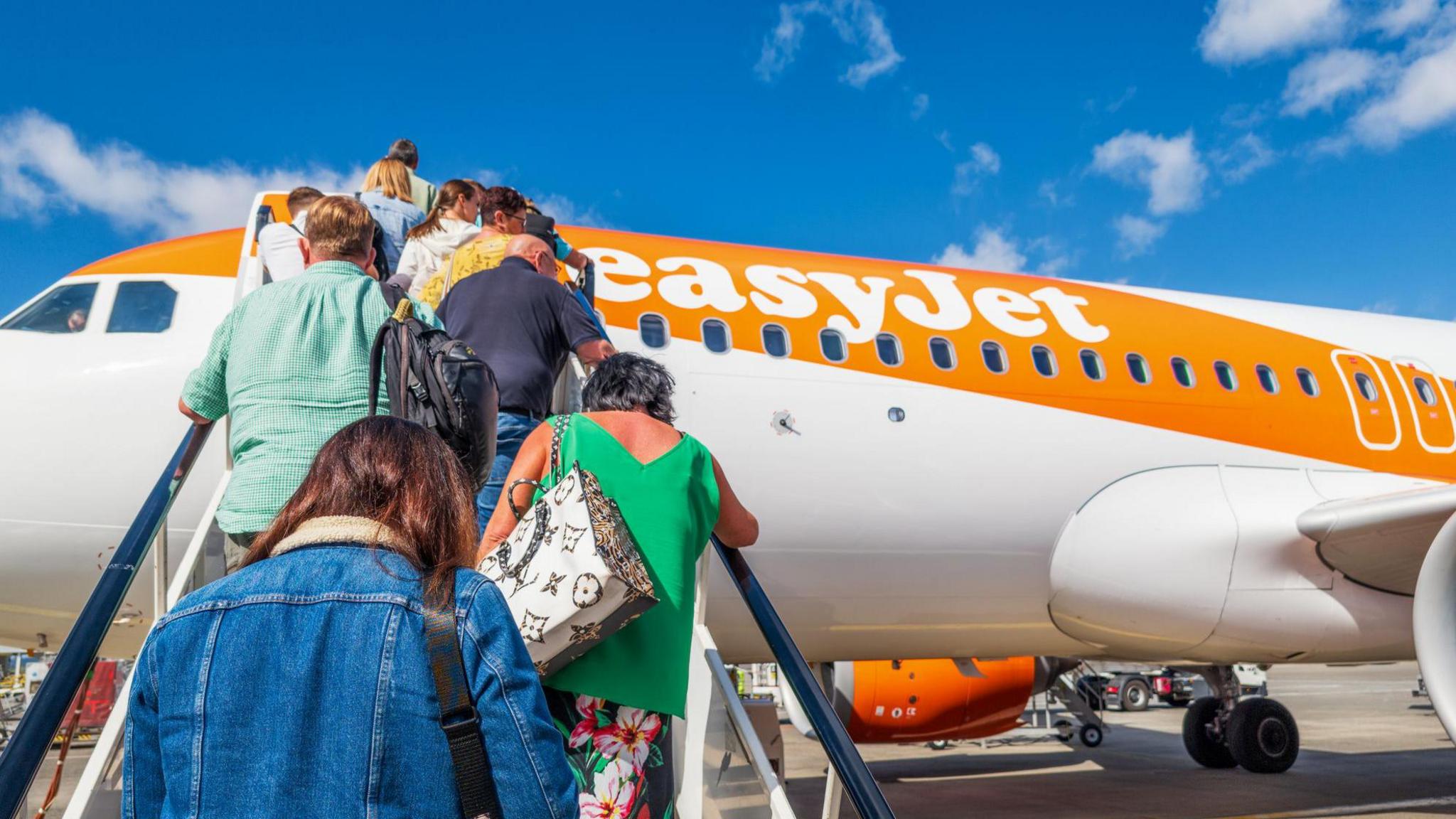 People climb the stairs onto an easyJet orange and white plane.