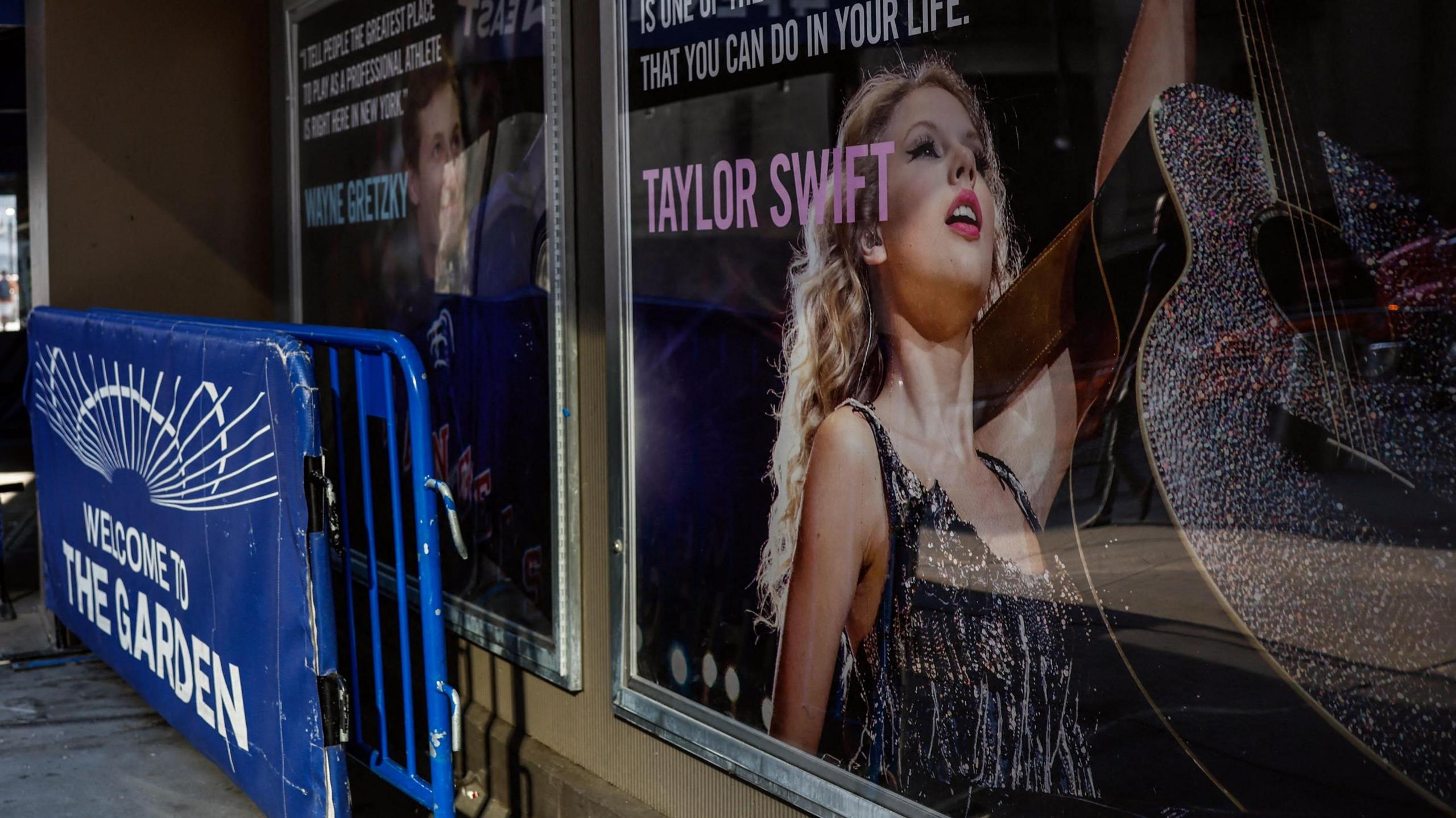 A poster of Taylor Swift  holding up a guitar outside Madison Square Garden, next to crush barriers saying "welcome to the Garden".