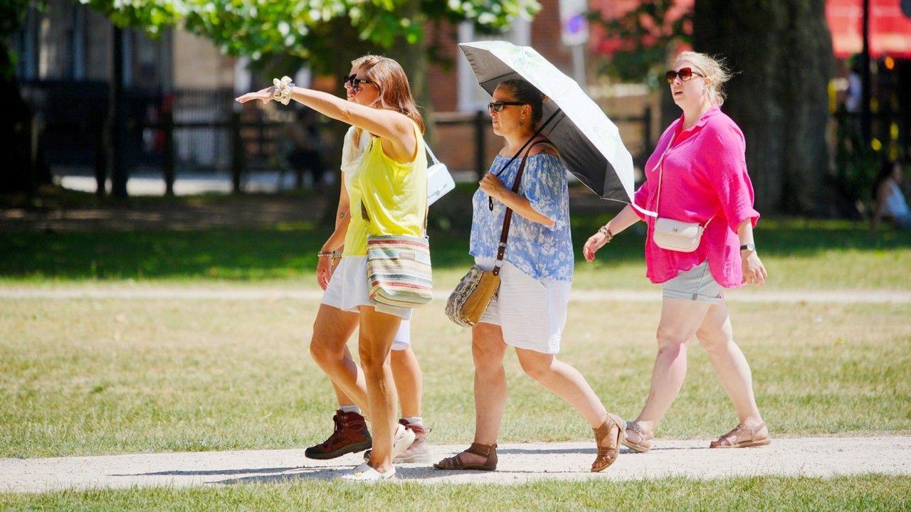 Four people strolling in the sunshine wearing shorts, one person is carrying an umbrella.