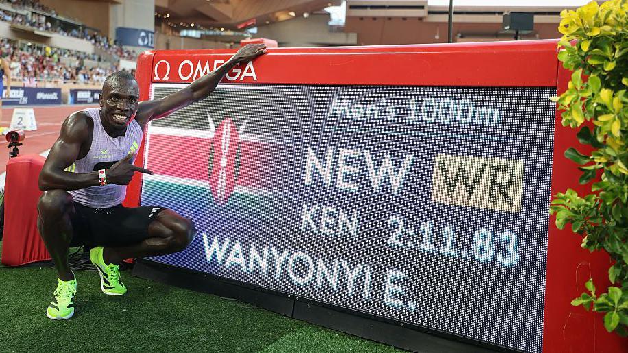 Emmanuel Wanyonyi poses for a photograph next to a digital screen showing his name and world record time after winning the 1,000m in Monaco