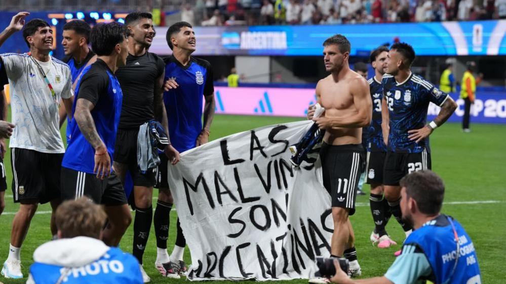 Several Argentinian football players standing on a pitch holding a banner saying "Las Malvinas Son Argentinas"