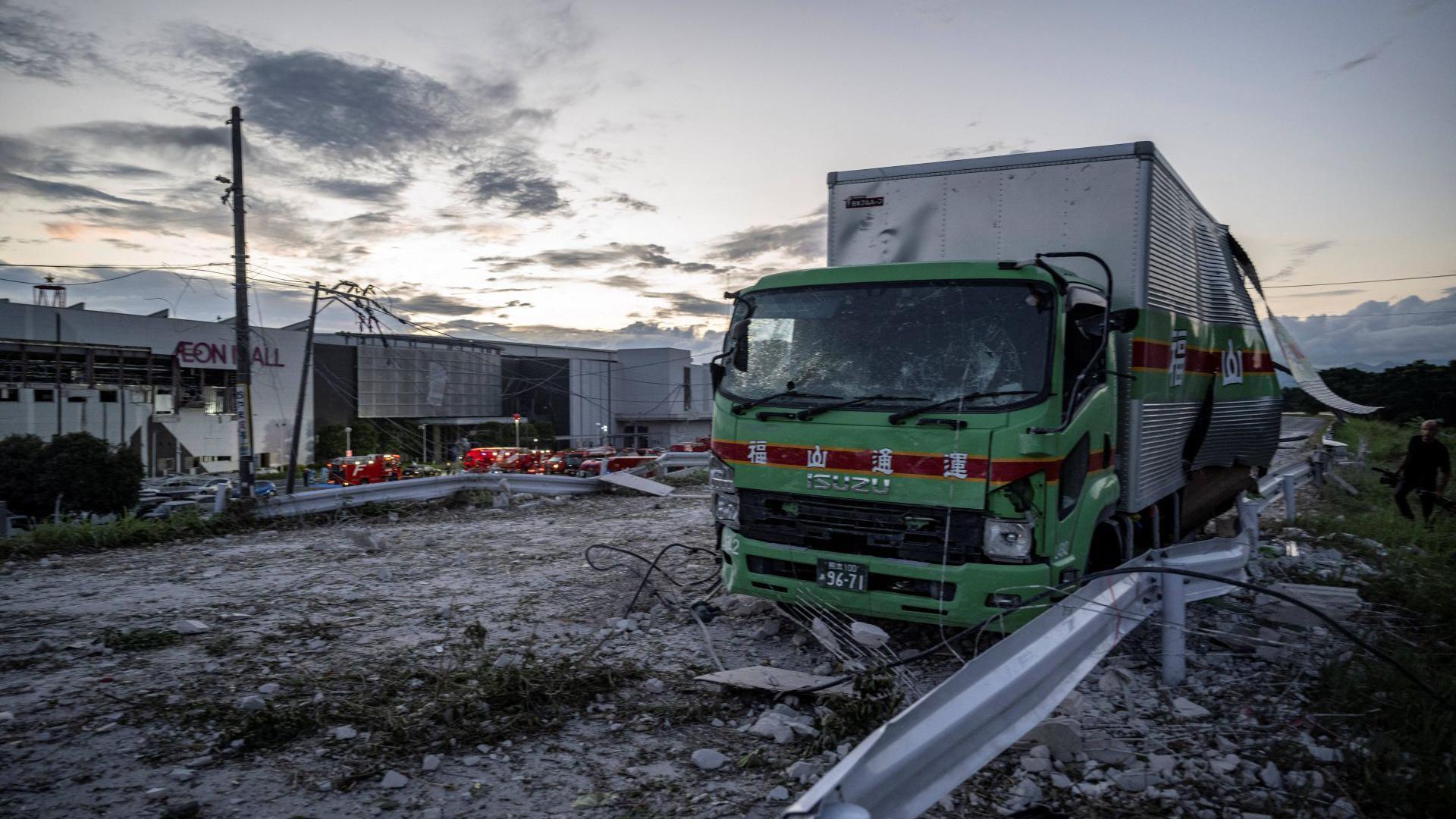 A damaged truck on a debris-covered road following an explosion at the Aeon Mall which is in the background