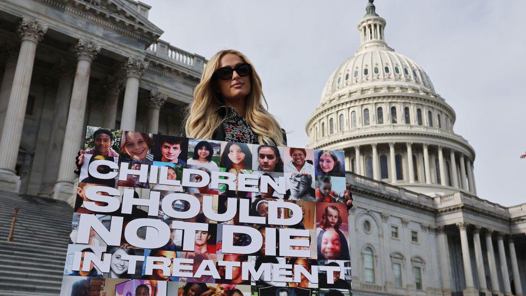 Celebrity hotel heiress Paris Hilton poses for photographs outside the US Capitol in December 2024 carrying a poster that says "Children should not die in treatment".