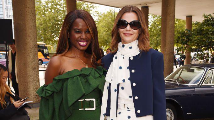 June Sarpong wearing a green off-the-shoulder dress with a large belt. She is standing next to Victoria Starmer who is wearing a navy jacket with white buttons and a white dress with blue spots.