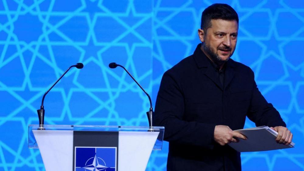 Zelensky leaves the podium holding a binder of notes