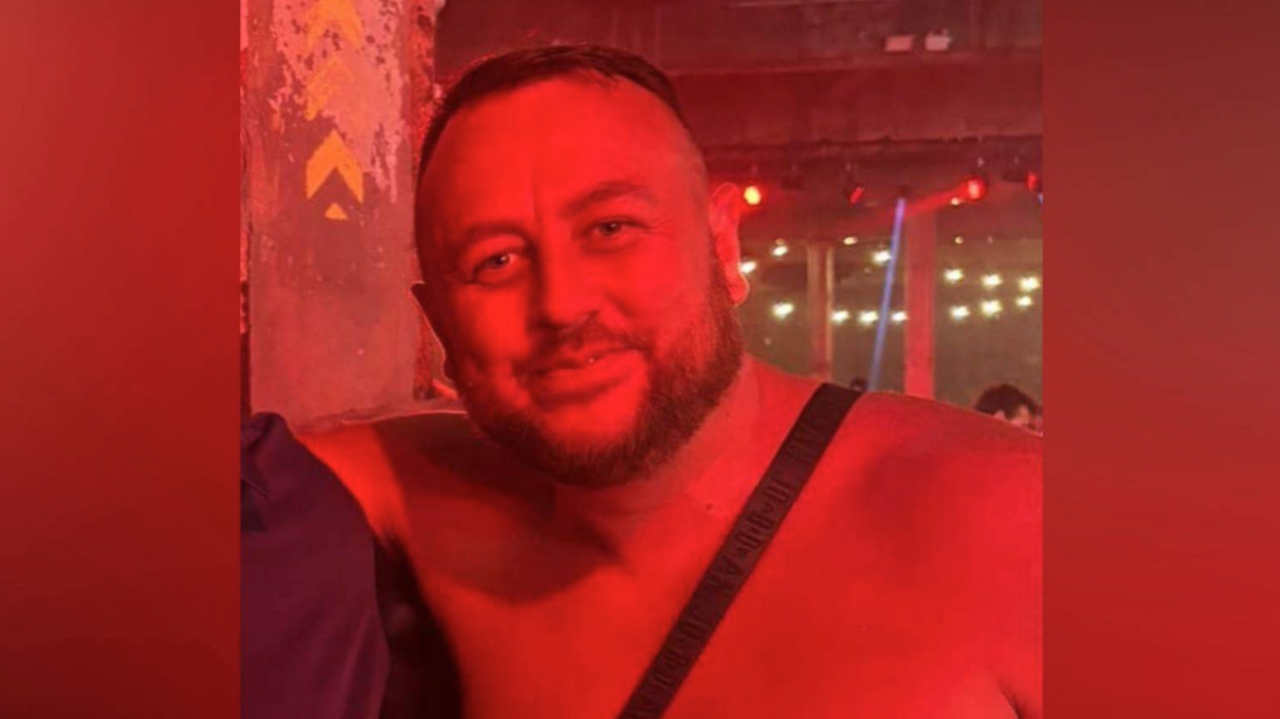 Head and shoulders shot of Sean in a red-lit nightclub or bar setting, he has short hair and a thin beard