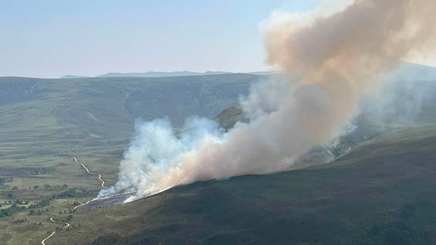 A green hill landscape with plumes of white smoke billowing into the air