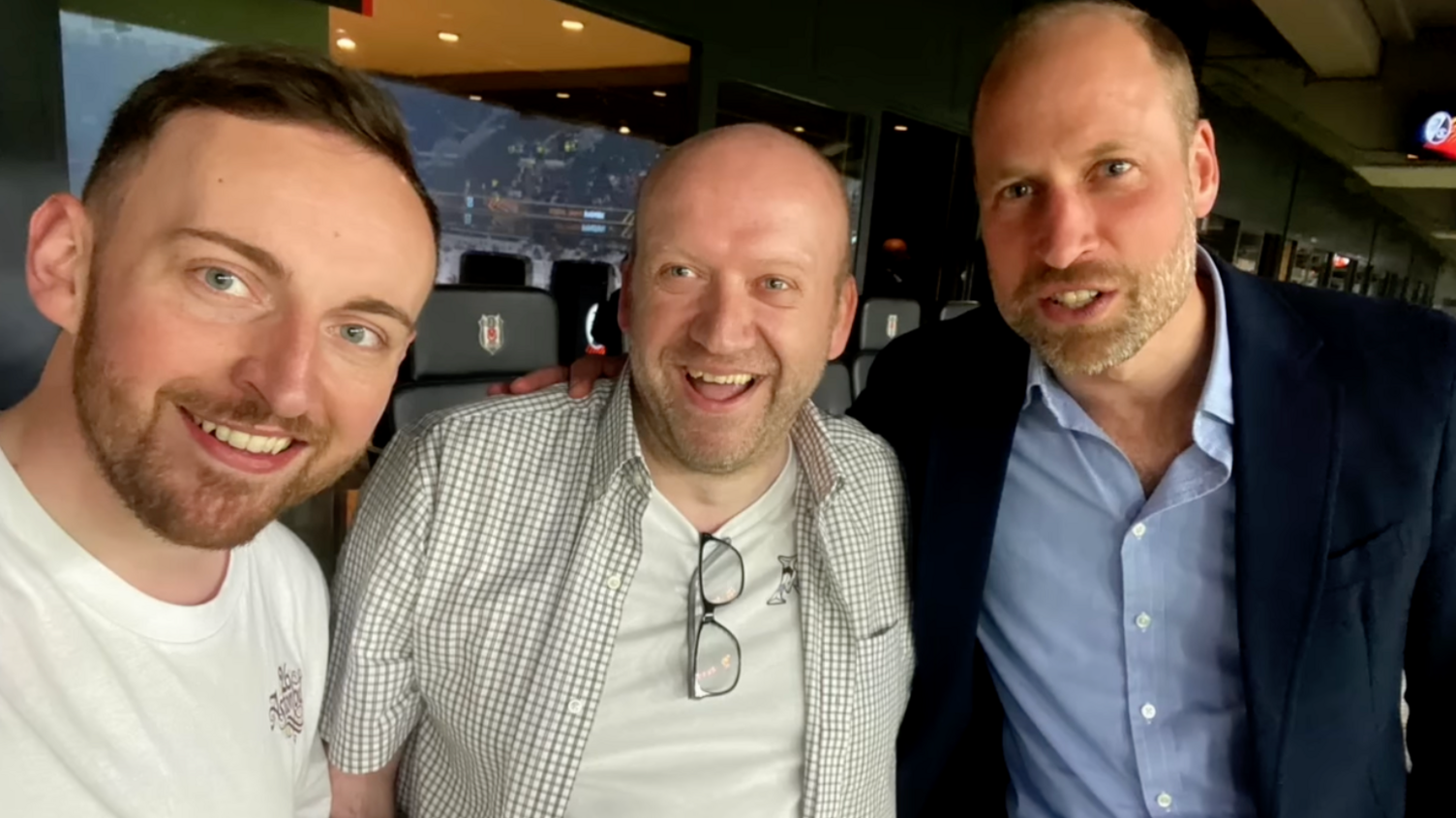 Prince William on the right of two men smiling inside a football stadium