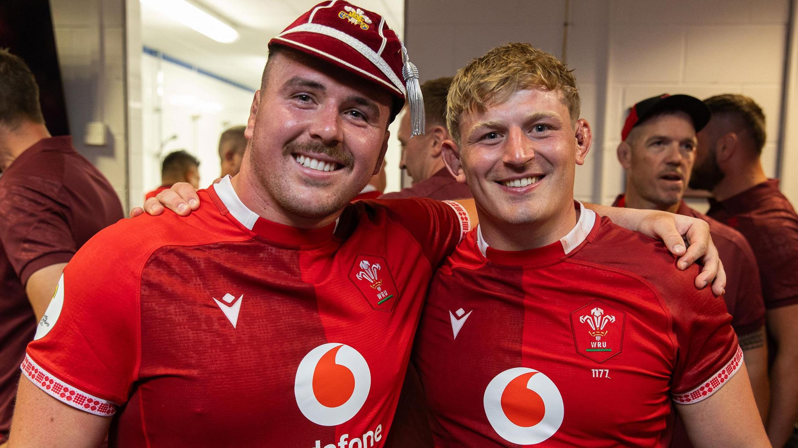 Wales flanker Jac Morgan (right) has his arm around the shoulder of Ben Warren (left) wearing a Wales cap as the pair pose for a photograph in Wales jerseys.