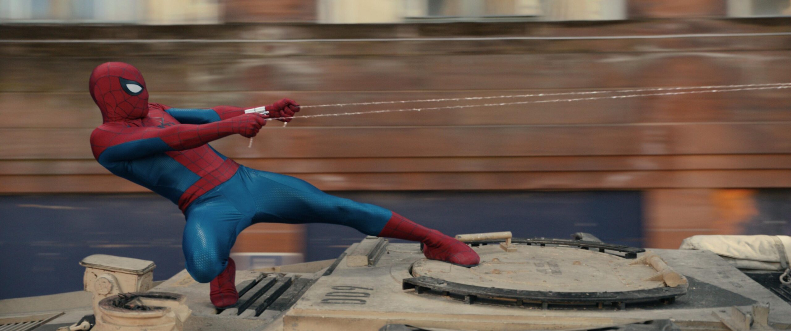 Spider-Man standing on top of tank and grabbing on to his web.