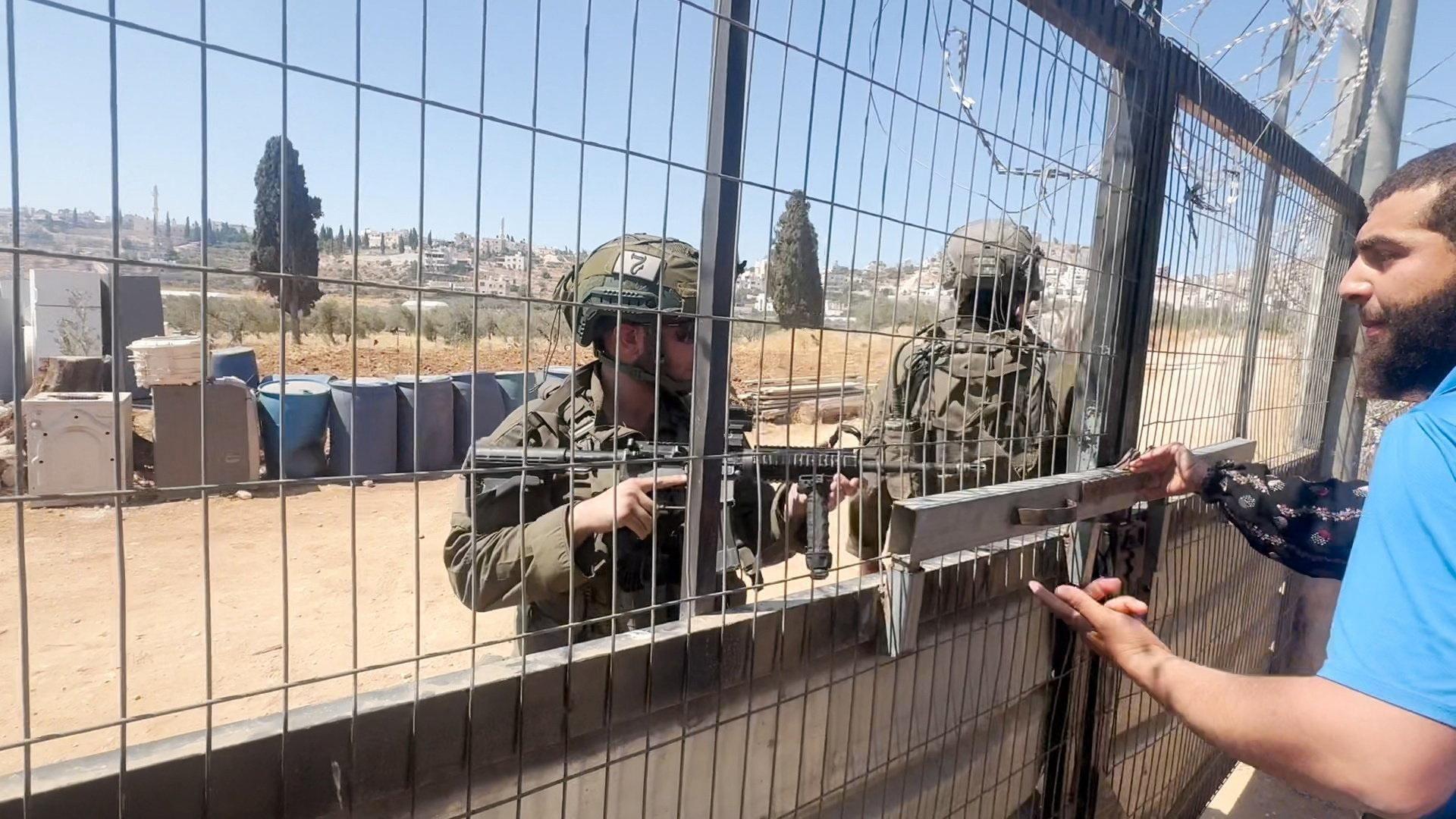 Screengrab from a video showing an Israeli soldier pointing his rifle towards a Palestinian woman and man as they stand behind a gate during a settler attack on a Palestinian home in the village of al-Mughayyir, near Ramallah, in the Israeli-occupied West Bank (11 July 2026)
