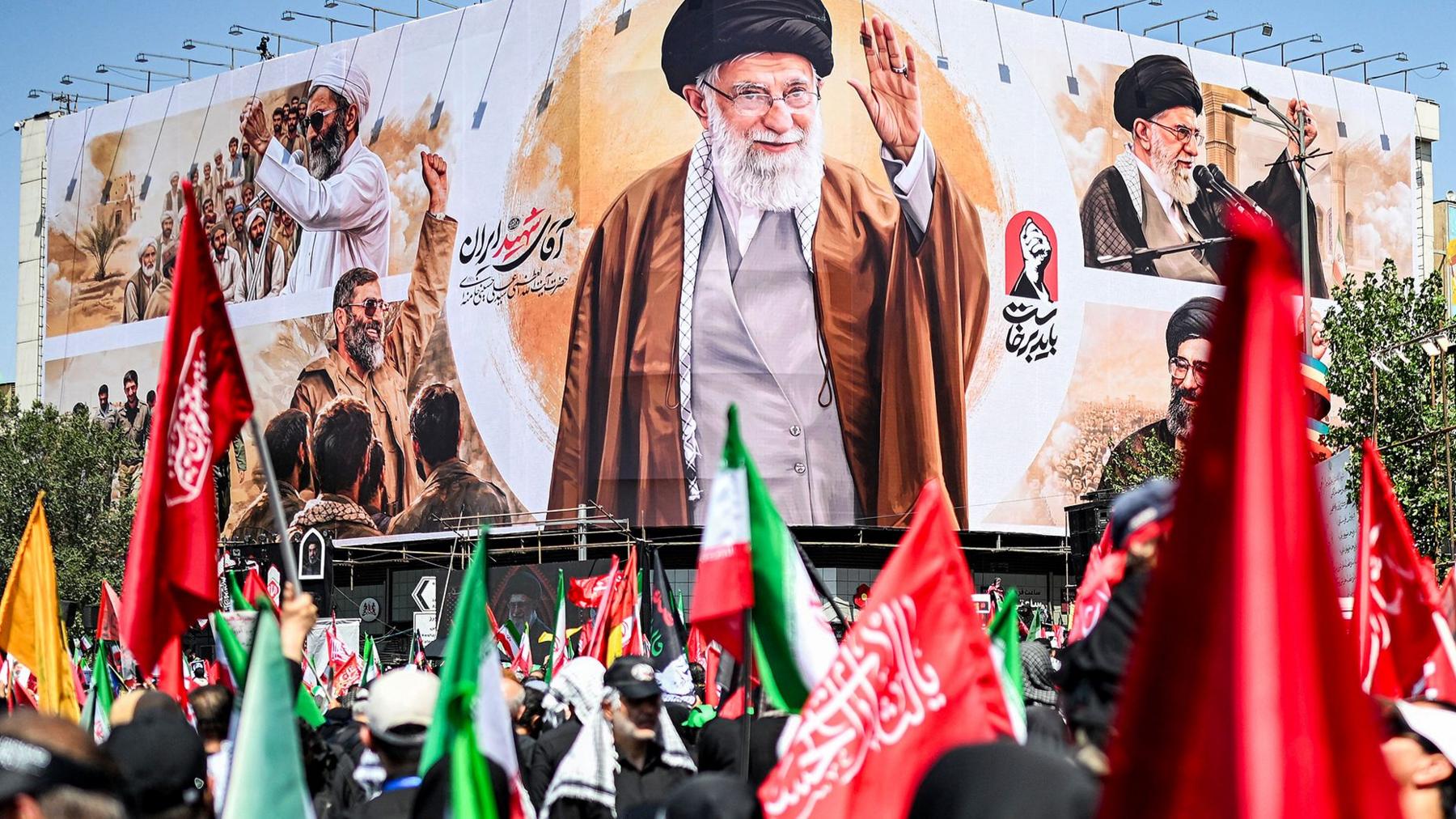 Crowds with Iranian flags in front of a billboard showing the late suprememe leader at his funeral