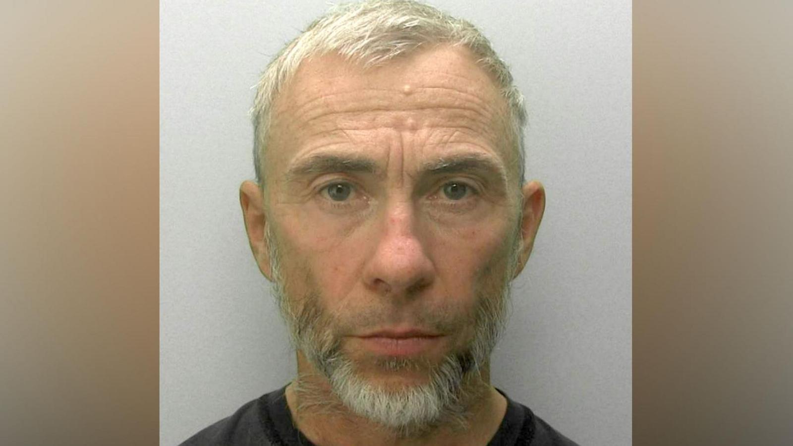 A police mugshot of James Holder. He has cropped grey hair and a short grey beard and is looking directly ahead.