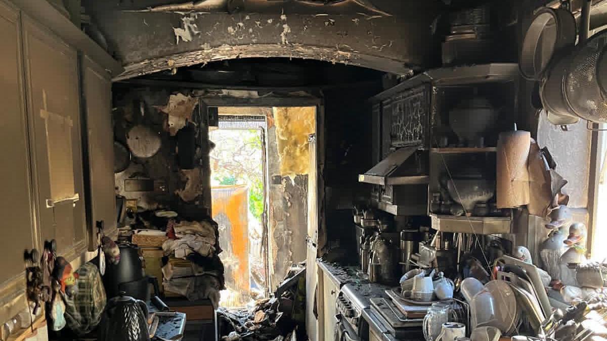 A kitchen with black soot and melted appliances and melted ceiling hanging down in the utility
