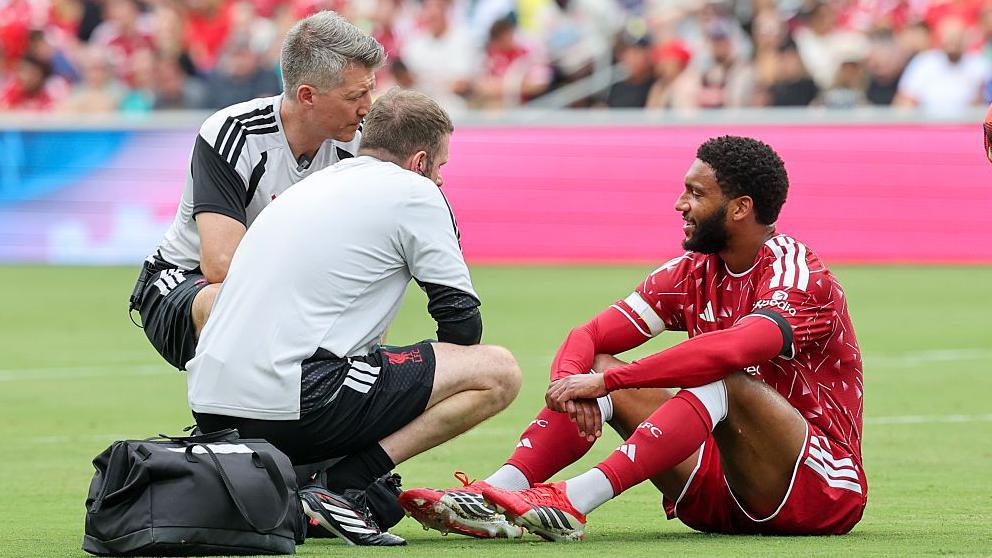 Joe Gomez, sitting on the pitch, is attended to by medical staff after an early injury against Sunderland