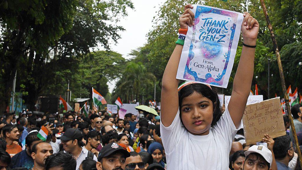 A young girl holds a placard as citizens gather to celebrate the resignation of Union Education Minister Dharmendra Pradhan.