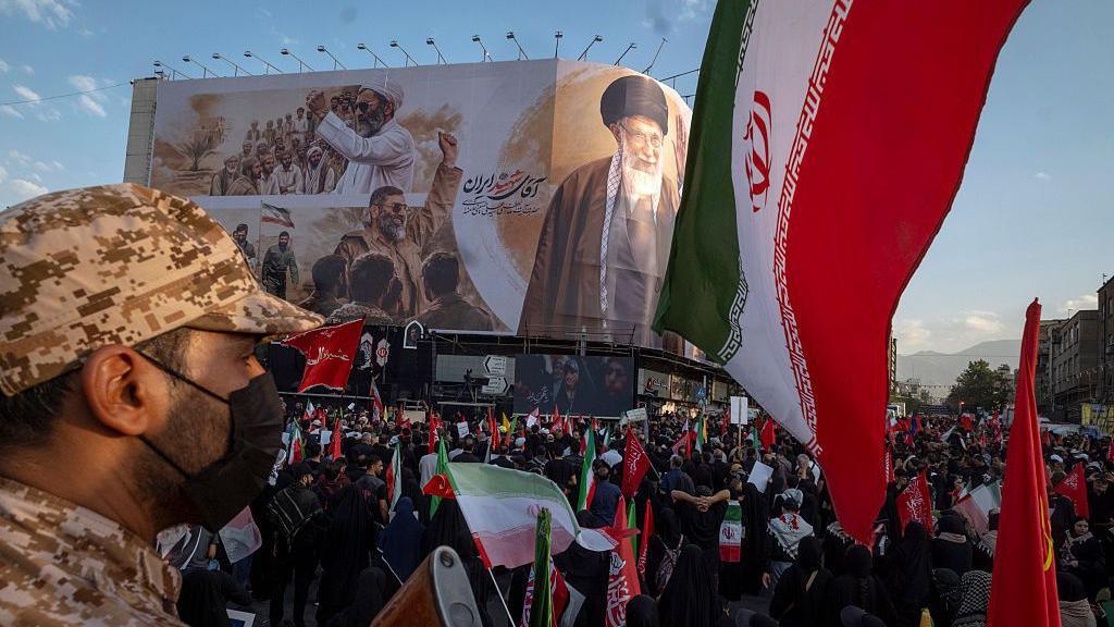 An armed member of the Islamic Revolutionary Guard Corps (IRGC) monitors the area while mourners participate in the funeral for the late Supreme Leader Ayatollah Ali Khamenei and his family in Tehran, Iran, on July 6, 2026.