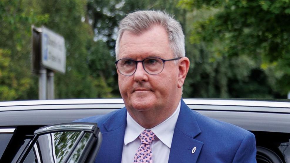 Jeffrey Donaldson has grey hair and is wearing glasses, a blue suit, white shirt and pink patterned tie, with a fish pin on his blazer.