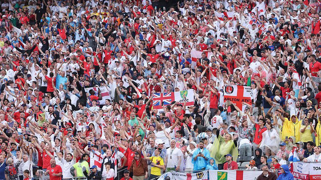 A large crowd of people holding flags of St George and Union Jack.