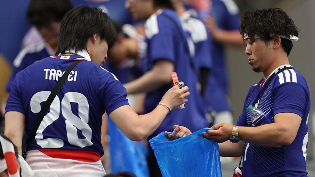 Two Japanese football plans cleaning a World Cup stadium and placing their trash in trash bags