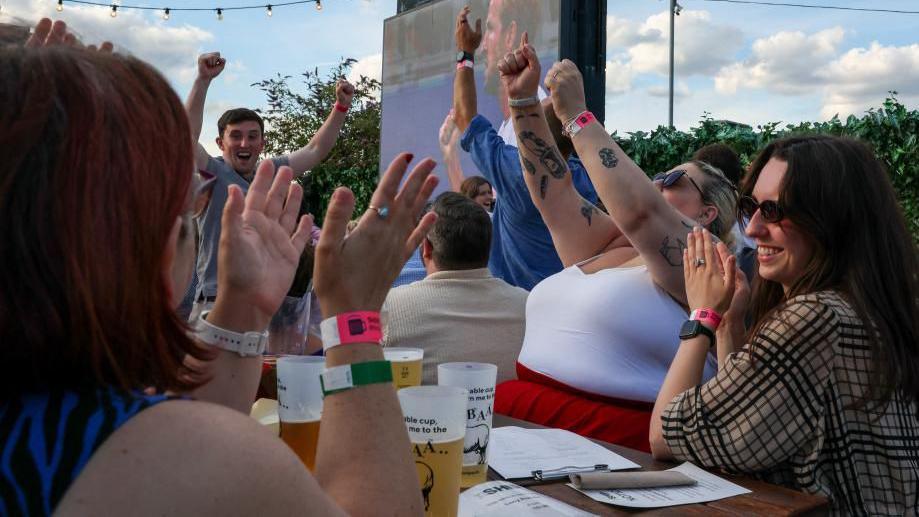 Fans cheer England's World Cup victory over DR Congo, watching a large screen showing Harry Kane, in a pub garden on Wednesday