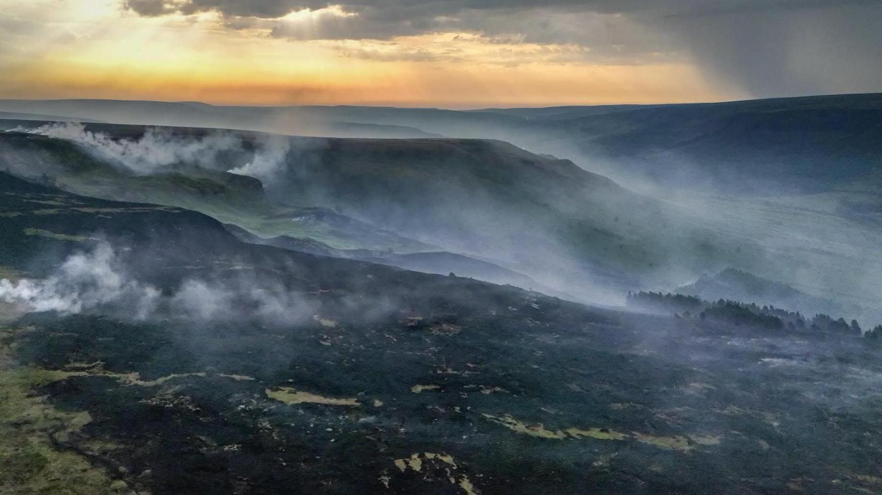 Shot of rolling moorland hills which are blackened and smoking