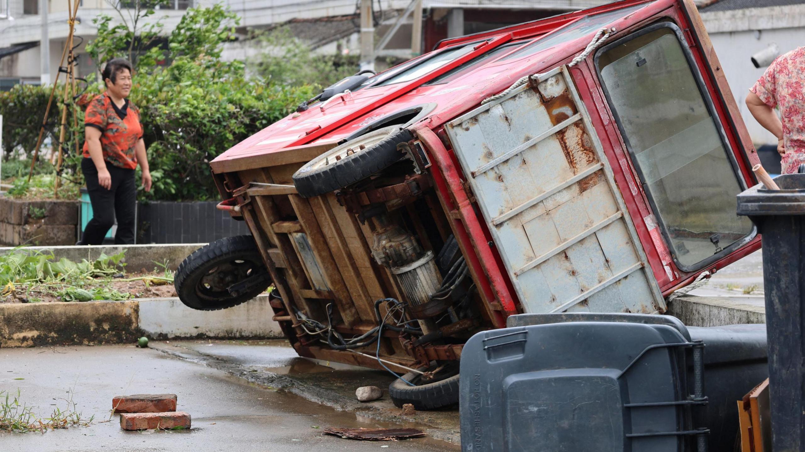 A woman walks past a vehicle knocked over by winds from Typhoon Bavi in Wenling, in China's eastern Zhejiang province on July 12, 2026.
