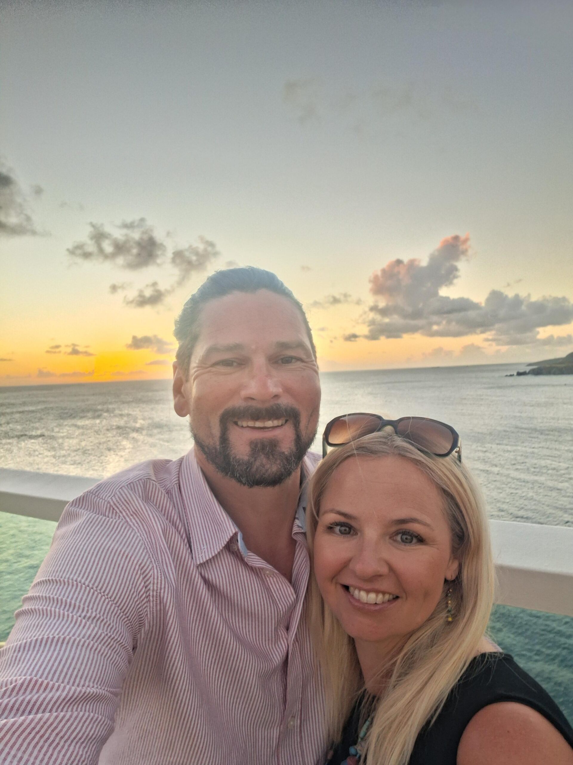 Man and woman smiling in front of the sea and sunset