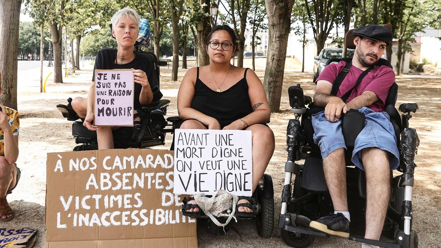 Protesters in wheelchairs  sitting outsode outside with signs that say "I am not a reason to die "