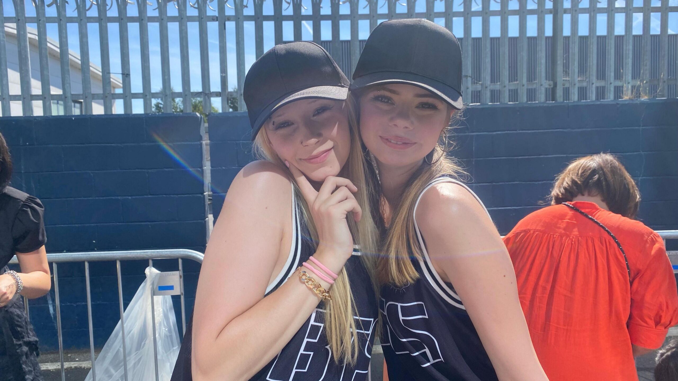 BTS fans Keira Mcalary and Jasmine Oliver stand in a queue outside Tottenham Hotspur Stadium, wearing BTS-branded basketball shirts