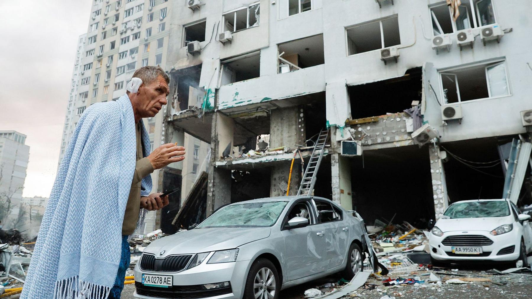 Injured man in a blue blanket standing outside a damaged building